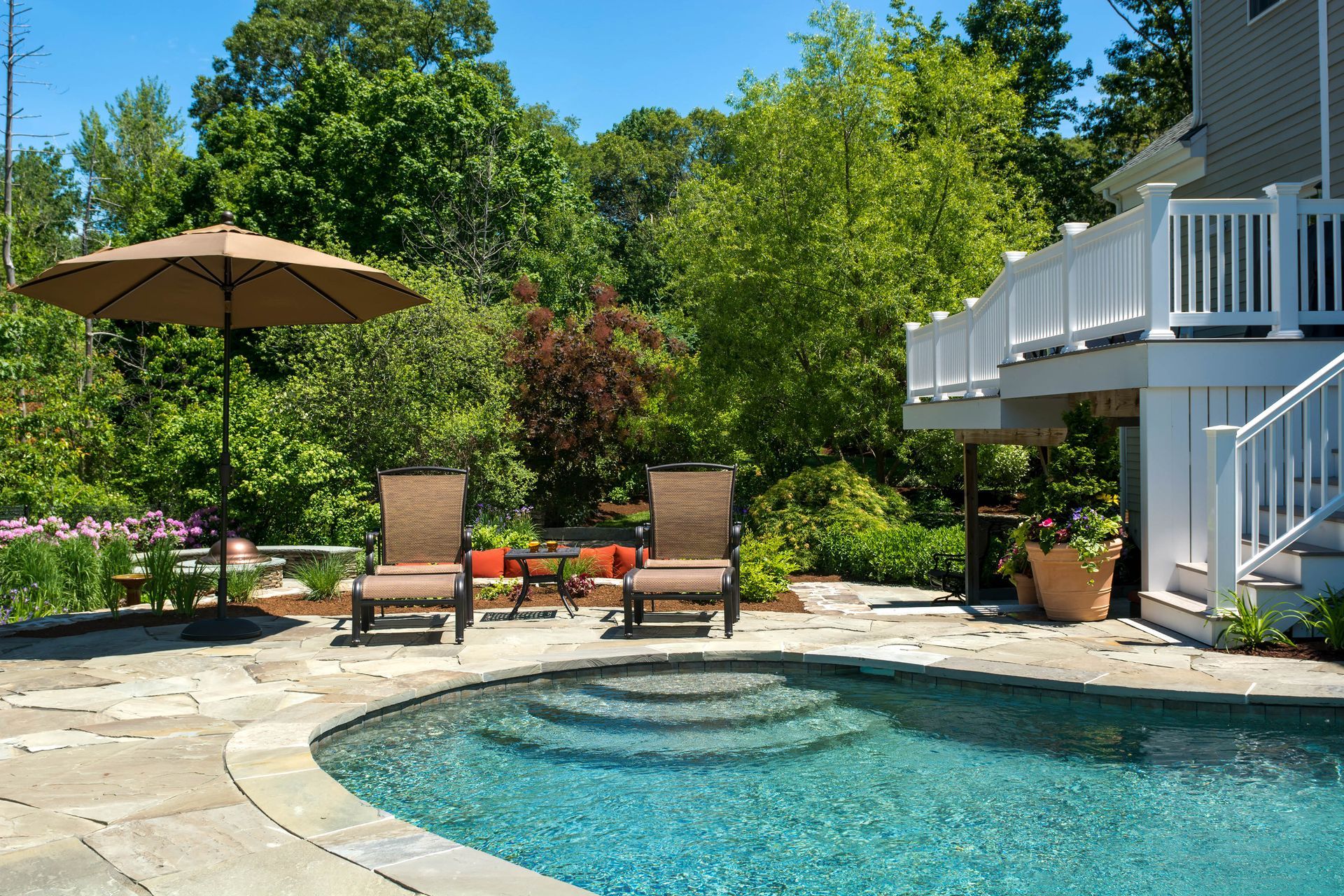 Backyard pool with lounge chairs, umbrella, and a deck, surrounded by trees.