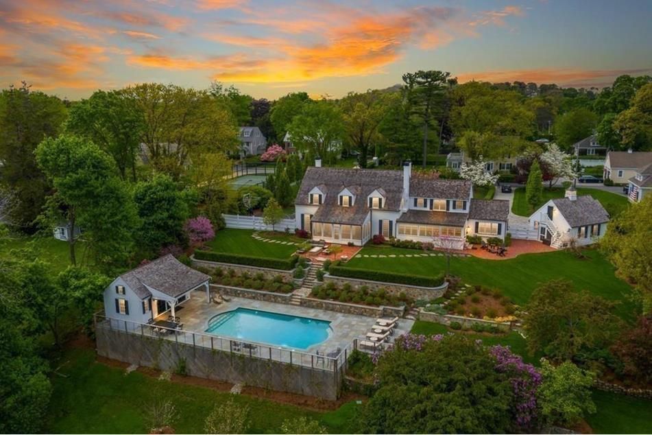 Aerial view of a large white house with a pool, set against a sunset sky.