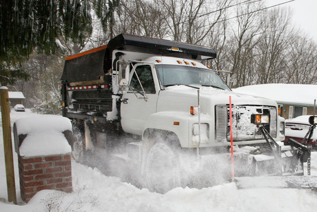 Snowplow clearing snow from a residential street. White truck plowing a layer of snow, winter scene.